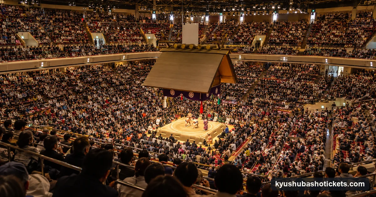 A packed sumo arena in the late afternoon, every seat full and the ring brightly lit as the last bouts begin