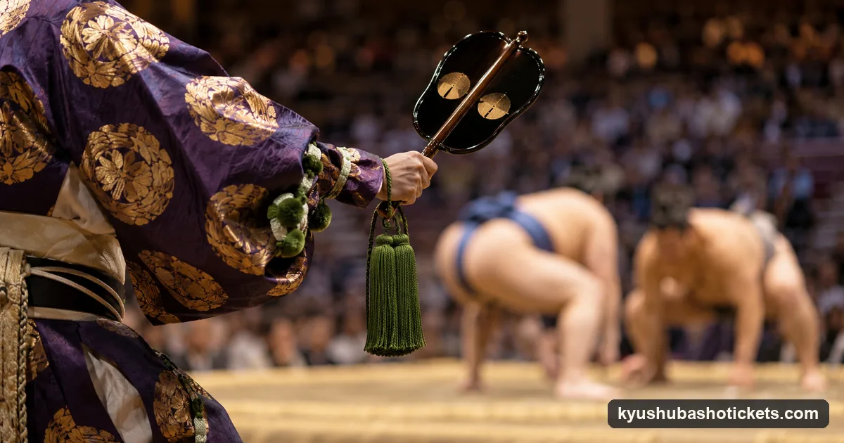 A sumo referee's hands raising a lacquered war fan with a long tassel, the wrestlers blurred behind