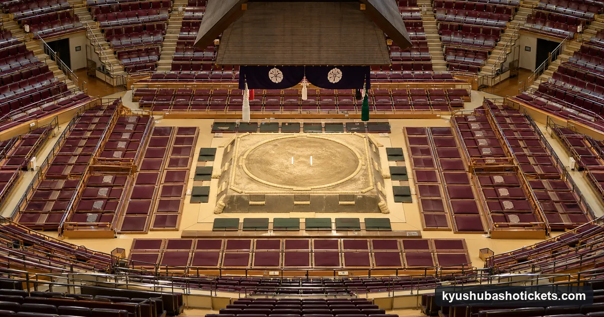 An overhead view of an arena floor with the square clay ring, box seats with cushions around it and chair seats in tiers
